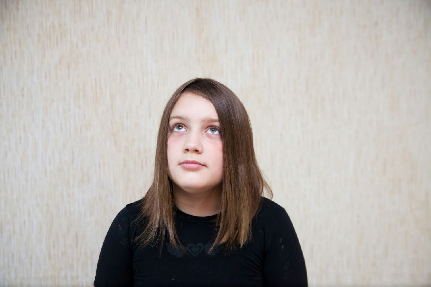 Tween girl with straight, light brown hair sits while looking up.